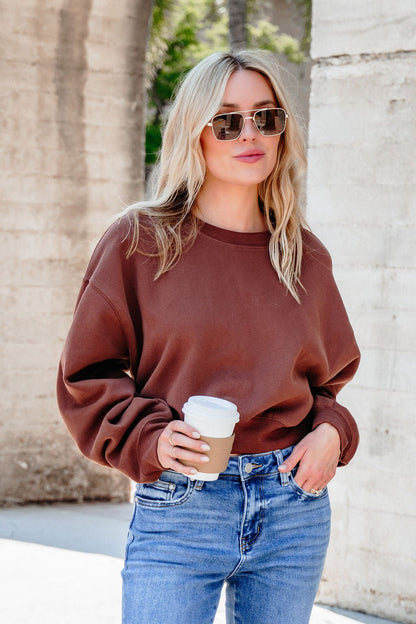 Woman wearing a Chestnut Crew Neck Ribbed Sweatshirt and sunglasses, holding coffee outdoors by a concrete wall.
