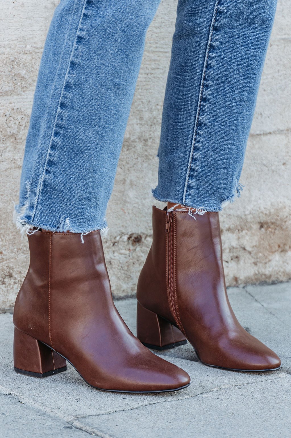 Chinese Laundry Davinna Ankle Booties with block heels and side zippers, styled with frayed-hem jeans on a concrete sidewalk.