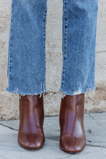 Person in frayed hem blue jeans and Chinese Laundry Davinna Ankle Booties stands on a sidewalk by a stone wall.