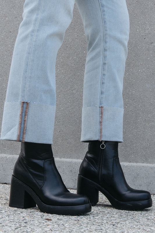 Model wears light-wash jeans with frayed hems and the Chinese Laundry Groovy Black Heeled Ankle Boots—FINAL SALE—on concrete.