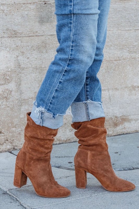 Wearing cuffed blue jeans and Chinese Laundry Kipper Brown Suede Heeled Boots—fall wardrobe essentials—on a concrete sidewalk.