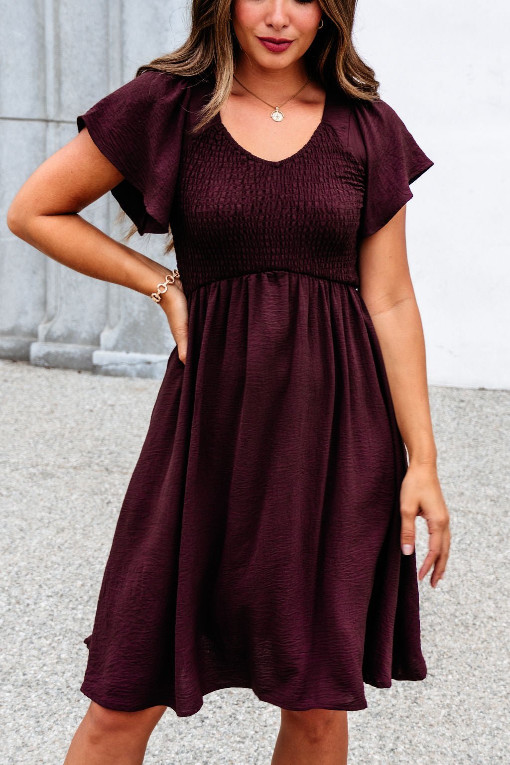 Woman wearing the Chocolate Brown Smocked Mini Dress - FINAL SALE, standing outdoors with one hand on her hip.