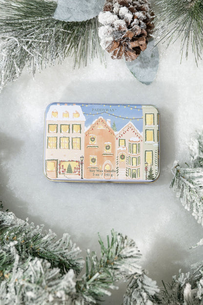 The Christmas Village Print Tin Soy Candle features pastel houses on snow, with frosted pine and a pinecone for a festive touch.