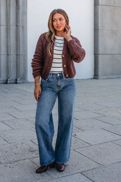 Woman outside in a Chunky Brown Button Down Cardigan, striped top, wide-leg jeans, and brown shoes, touching her hair.