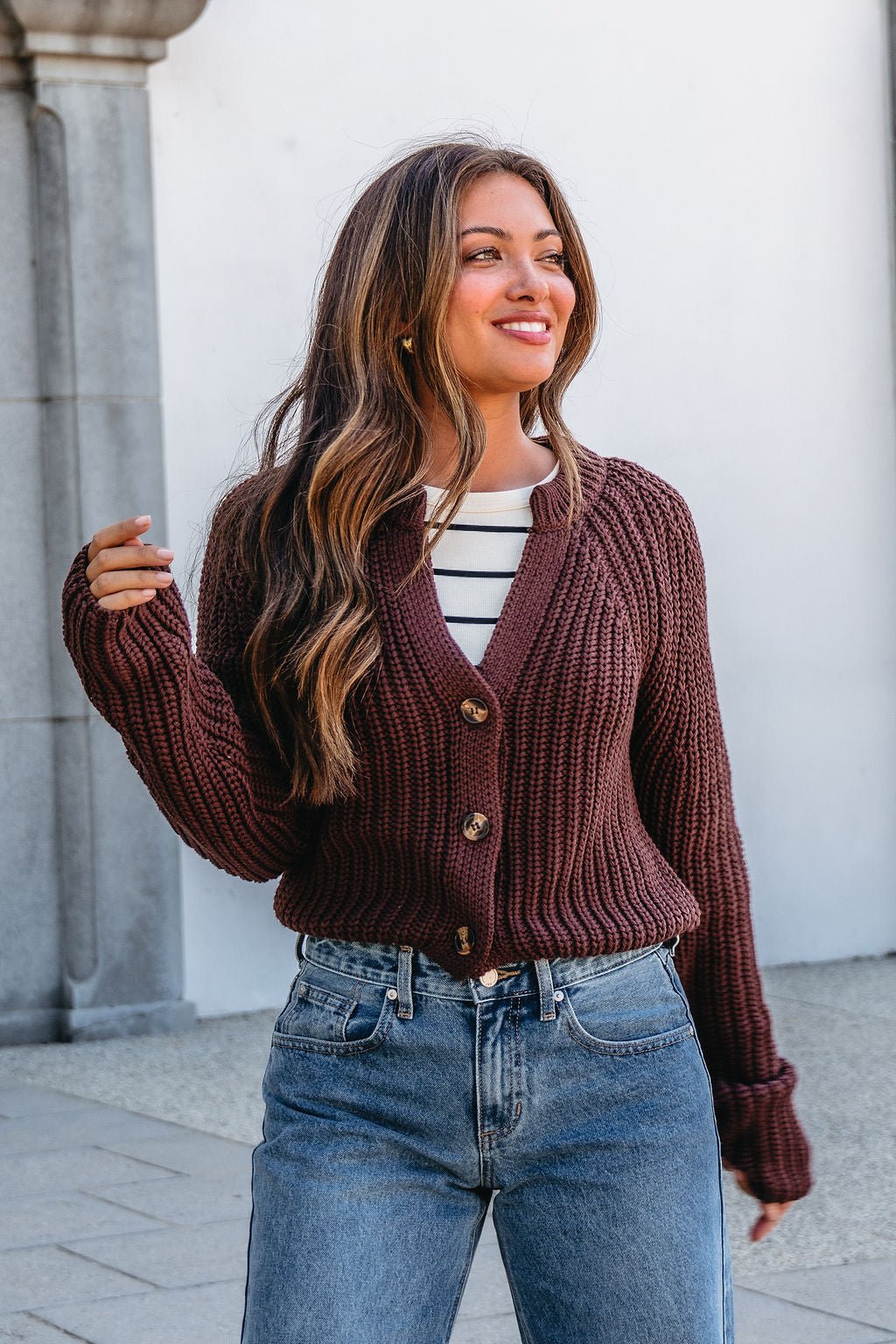 Woman wearing a Chunky Brown Button Down Cardigan over a striped shirt and blue jeans, smiling outdoors.