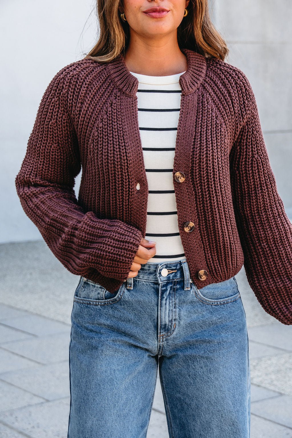 Woman wearing a Chunky Brown Button Down Cardigan over a striped top with blue jeans, standing outdoors.