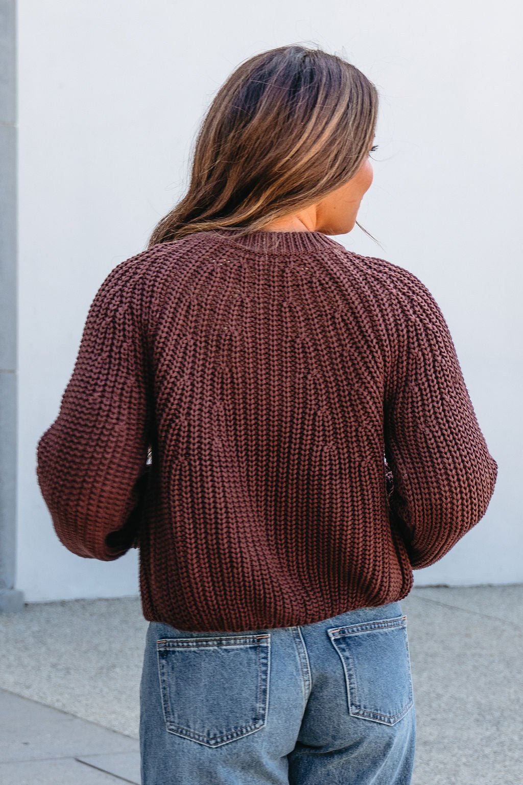 Woman with long brown hair wears the Chunky Brown Button Down Cardigan and blue jeans outdoors, seen from behind. Magnolia Exclusive.