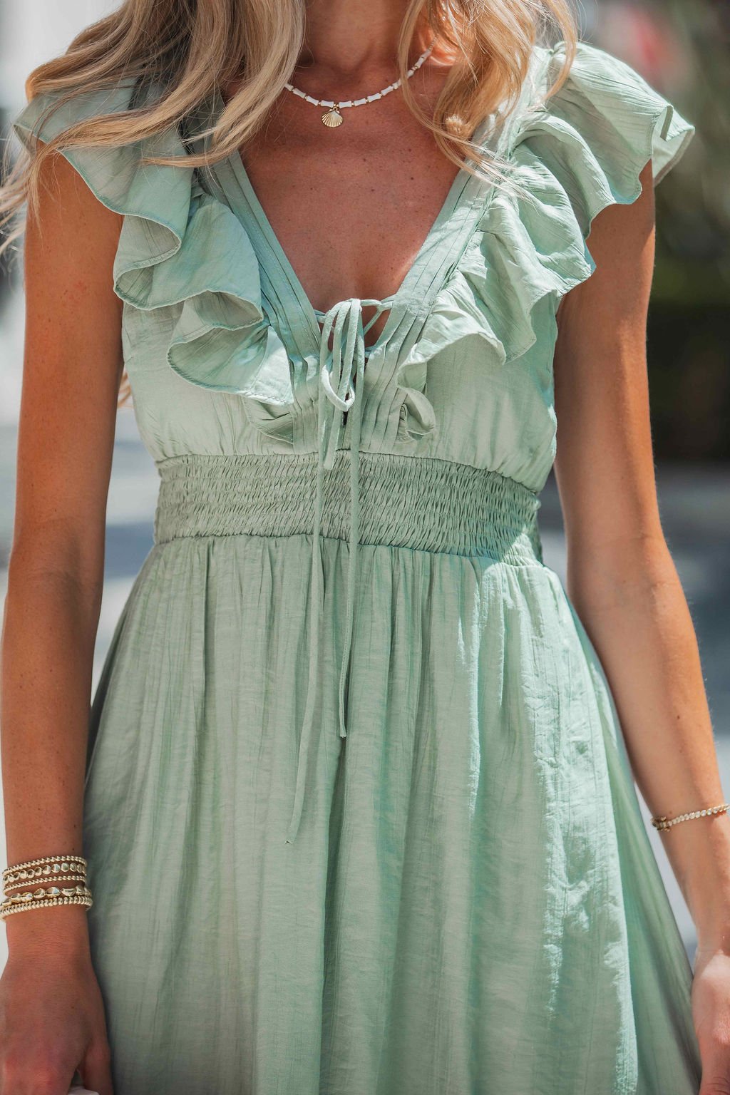 A woman stands outdoors in the Classic Sage Ruffled Midi Dress, styled with layered necklaces and gold bracelets.