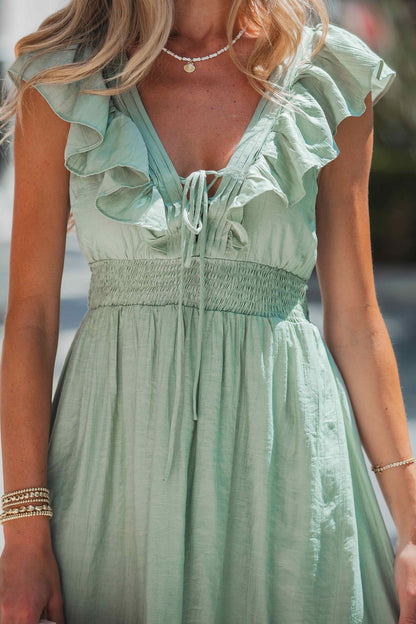 A woman stands outdoors in the Classic Sage Ruffled Midi Dress, styled with layered necklaces and gold bracelets.