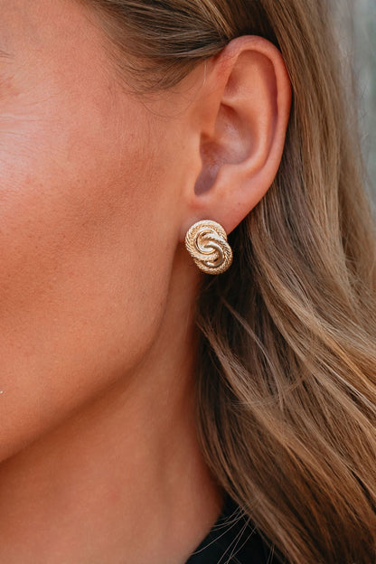 Close-up of a woman's ear wearing Coastal Gold Interlink Earrings; her wavy brown hair is visible.