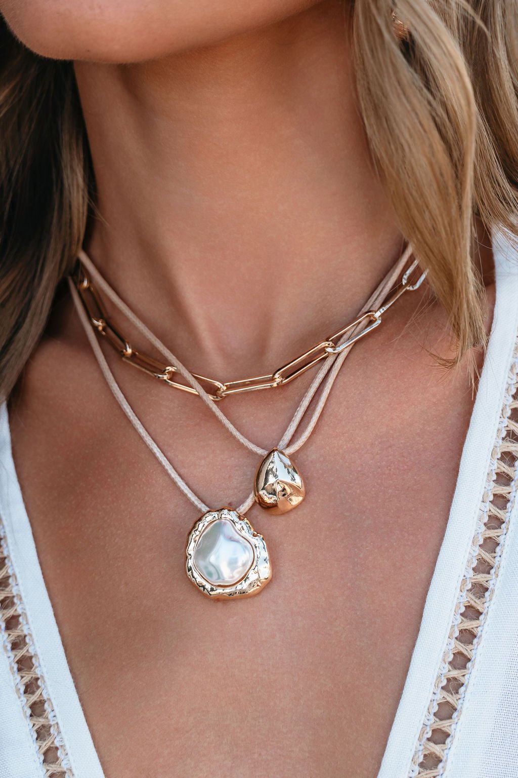 A woman wears the Coastal Lux 3 Layered Necklace of gold and pearls with a white textured top with crochet trim.