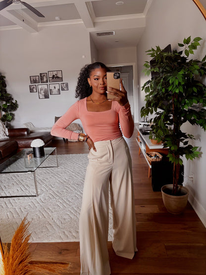 A woman in a pink top and Collins Cream Wide Leg Trousers takes a mirror selfie in a stylish living room with plants and photos.
