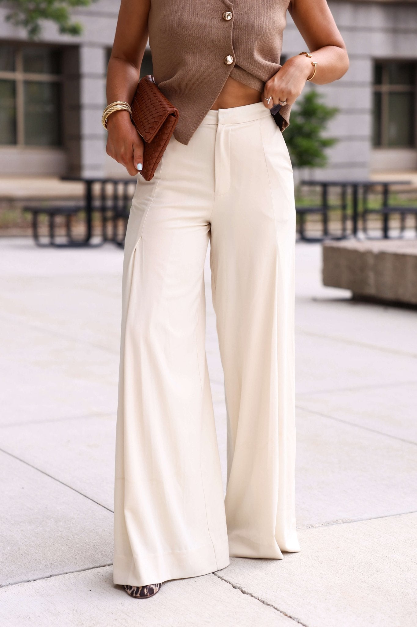 Woman in Collins Cream Wide Leg Trousers stands outdoors, styled chicly with a brown sleeveless top and clutch—perfect workwear.