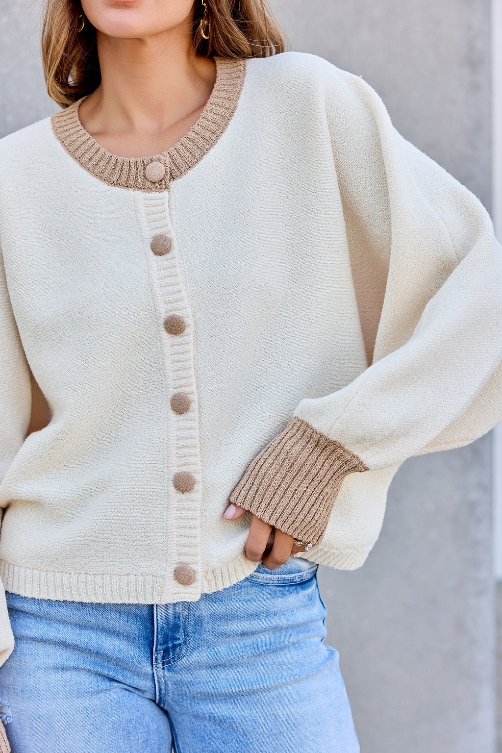 Woman in Contrast Ribbed Cardigan - Cream with tan trim and light blue jeans, standing against a gray background.
