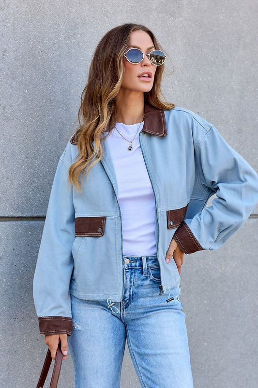 Woman in sunglasses wears the Contrast Trim Jacket - Dusty Blue over a white shirt and jeans, standing against a gray wall.