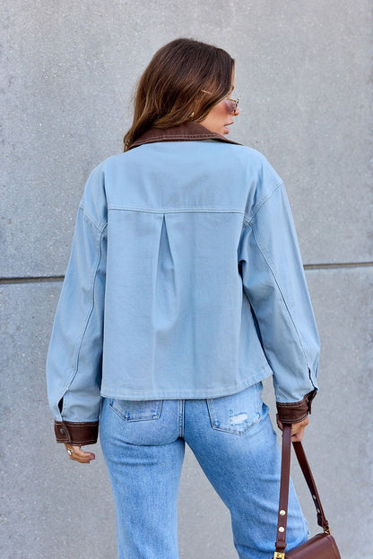 Woman in Contrast Trim Jacket - Dusty Blue | Pre Order, jeans, and brown purse stands against gray concrete wall, facing away.