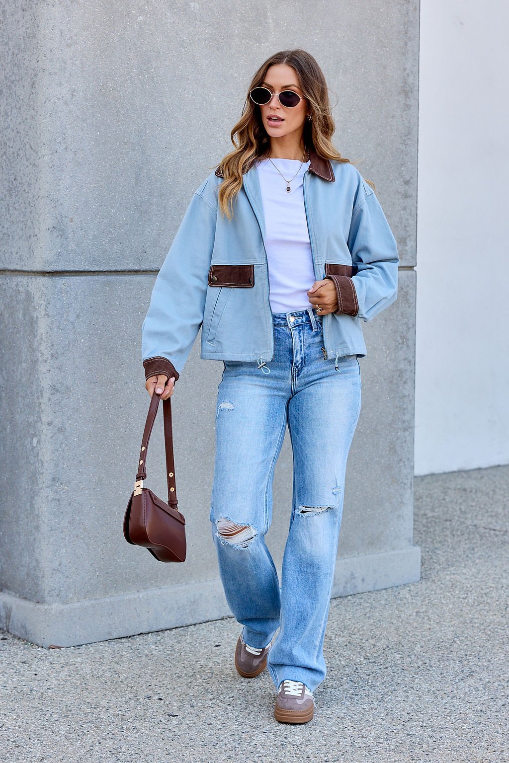 Woman in sunglasses, Contrast Trim Jacket - Dusty Blue, white top, ripped jeans, brown handbag on the sidewalk.