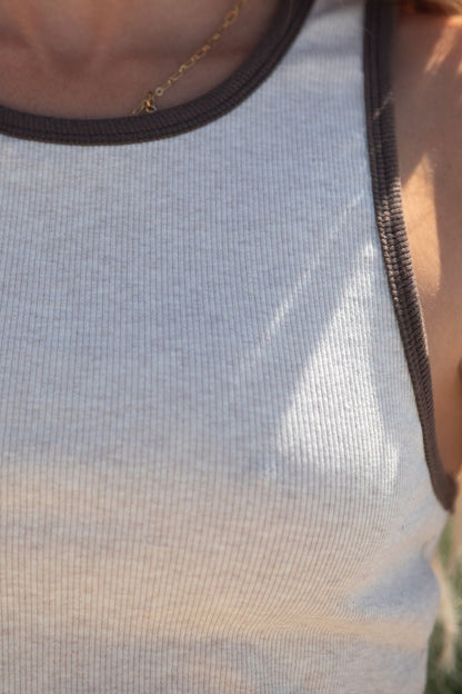 Close-up of a person wearing the Contrast Trim Tank Top - Ivory, featuring ribbed detailing and a thin gold necklace.