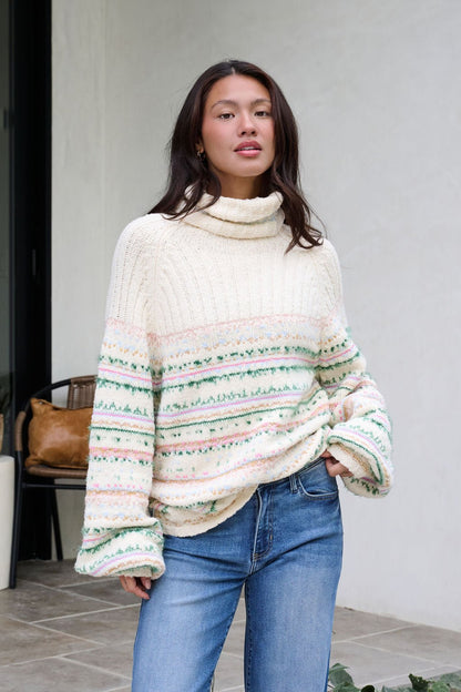 A woman in a Cozy Cream Turtleneck Striped Sweater and blue jeans radiates holiday style outdoors by a light wall.