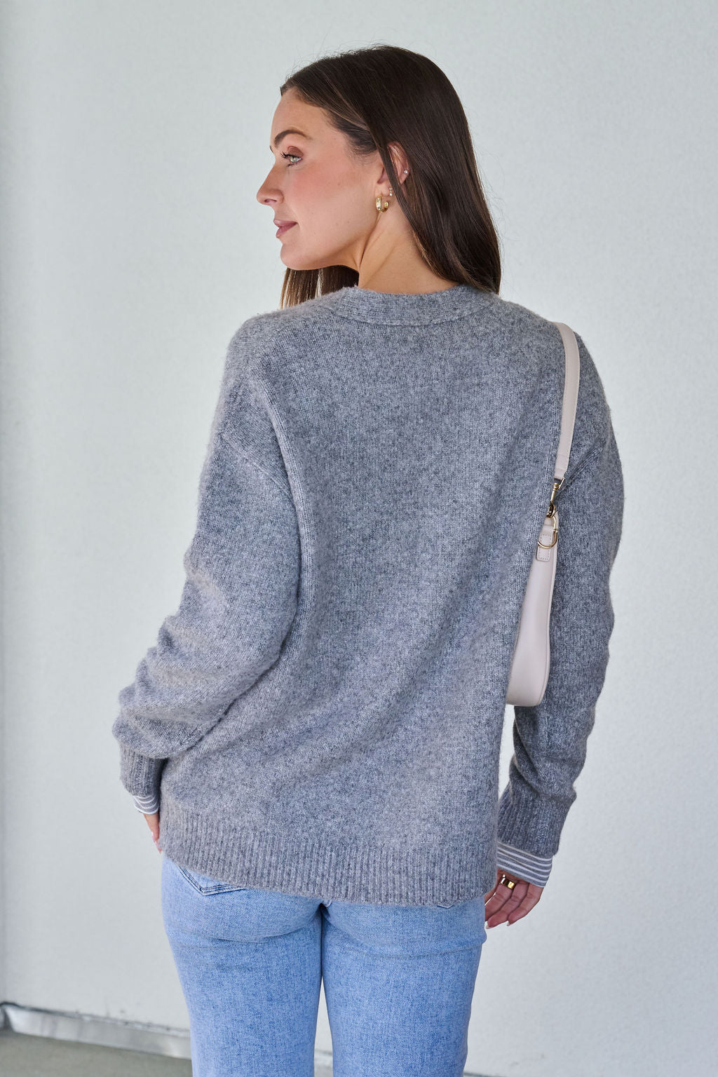 Woman with long brown hair wears the Cozy Grey Boyfriend Cardigan and light blue jeans, looking over her shoulder.