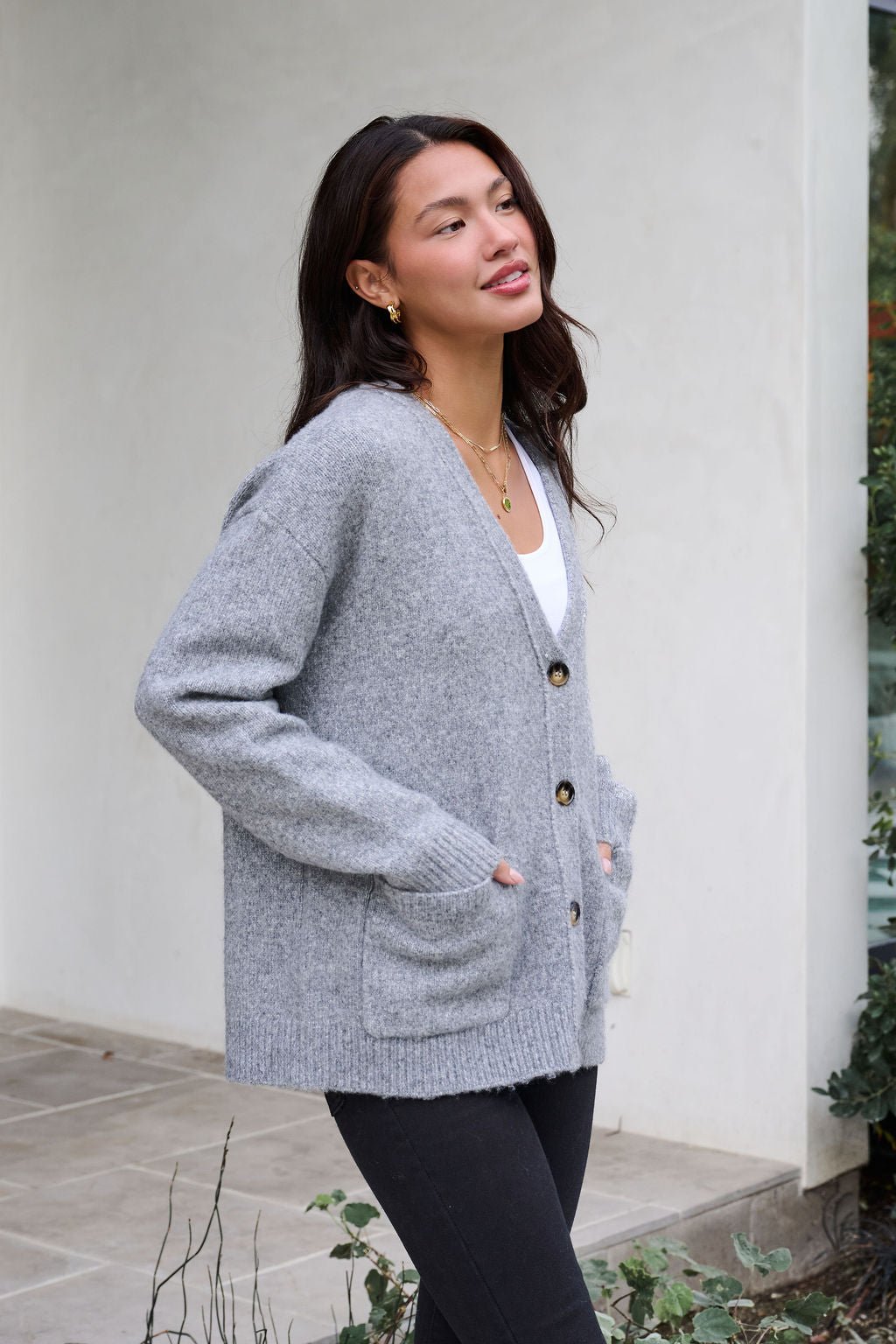 Woman outdoors wearing the Cozy Grey Boyfriend Cardigan over a white top and black pants, hands in cardigan pockets.