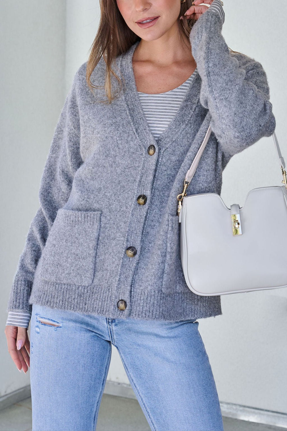 Woman in Cozy Grey Boyfriend Cardigan - FINAL SALE, striped top, light blue jeans, carrying a white handbag.
