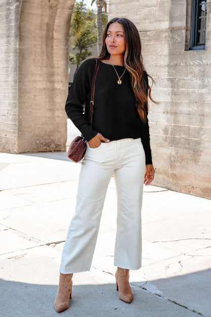 Woman outside in the Cozy Ribbed Boat Neck Sweater - Black, white pants, brown heels, shoulder bag, pendant necklace.