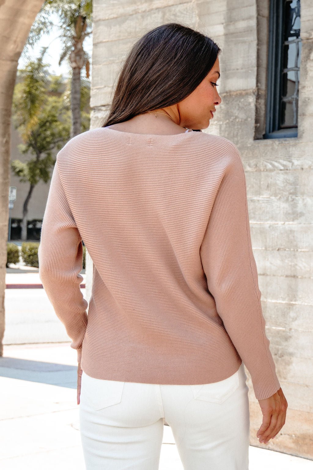 A woman with long brown hair wears the Cozy Ribbed Boat Neck Sweater in camel, standing outdoors with her back to the camera.