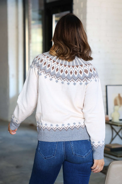 A woman in a cream and grey Aztec Print Sweater from the autumn collection stands indoors with her back to the camera.