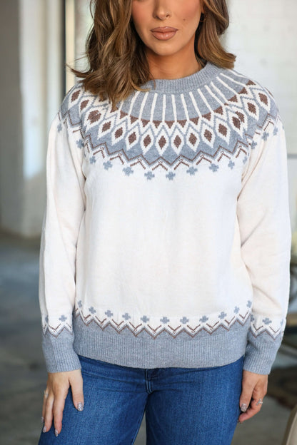 Woman wearing a Cream and Grey Aztec Print Sweater with jeans indoors, her hair styled in loose waves.