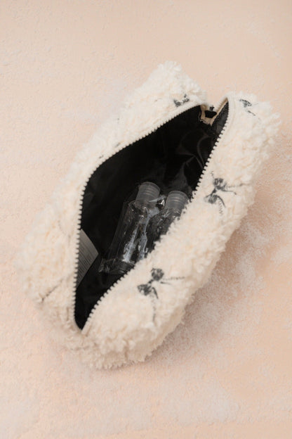 The Cream Cherie Sherpa Cosmetic Pouch Bag in white with black lining, shown partially open with two clear bottles inside.