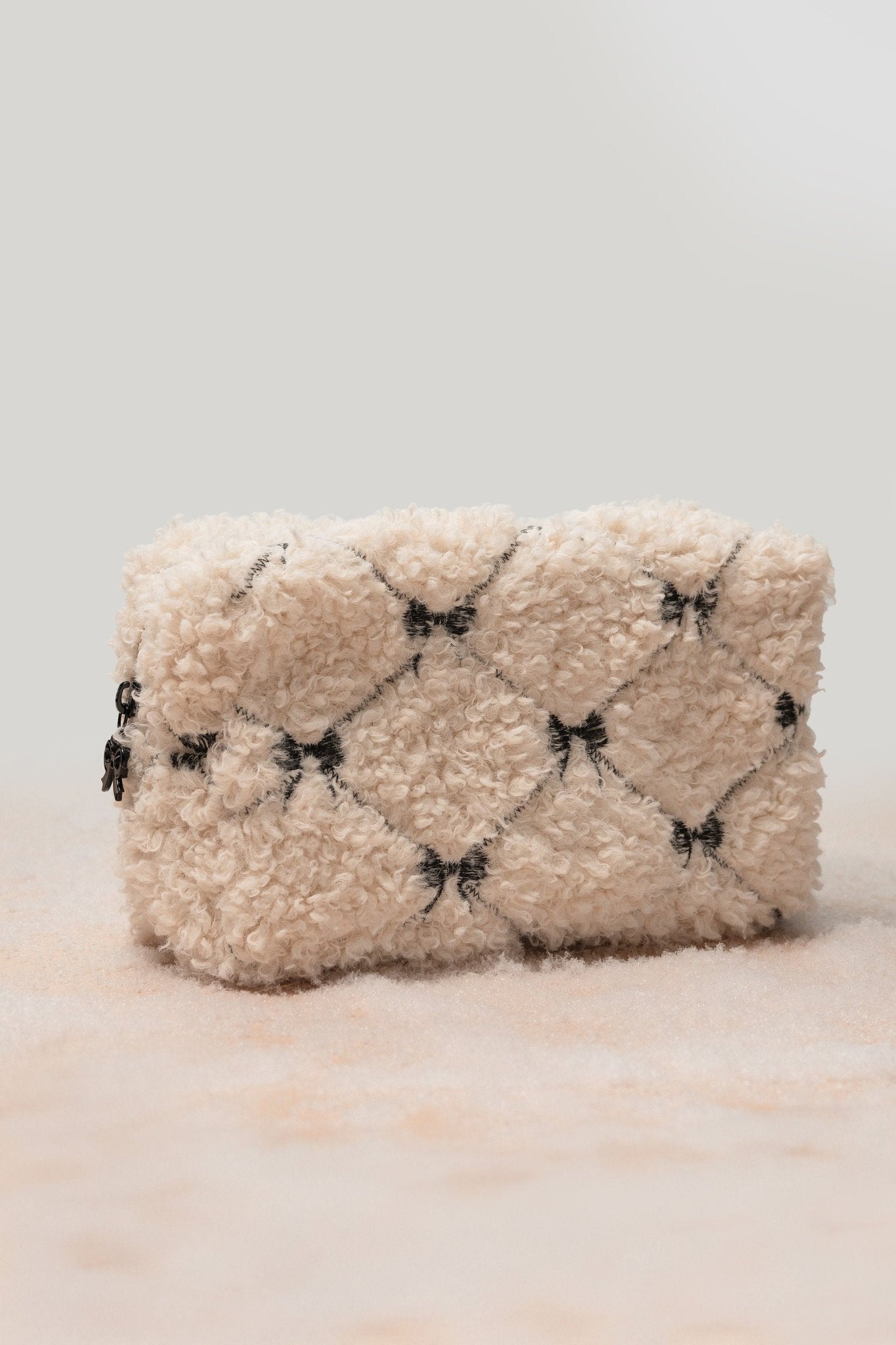 The Cream Cherie Sherpa Cosmetic Pouch Bag features a quilted cream design with black bows—ideal for gifting or travel.