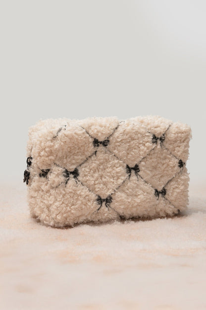 The Cream Cherie Sherpa Cosmetic Pouch Bag features a quilted cream design with black bows—ideal for gifting or travel.