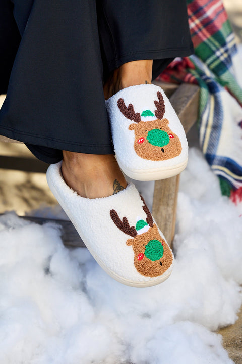 Person wearing Cream Faux Plush Reindeer Slippers sits on a chair with a plaid blanket—perfect as a Christmas gift.