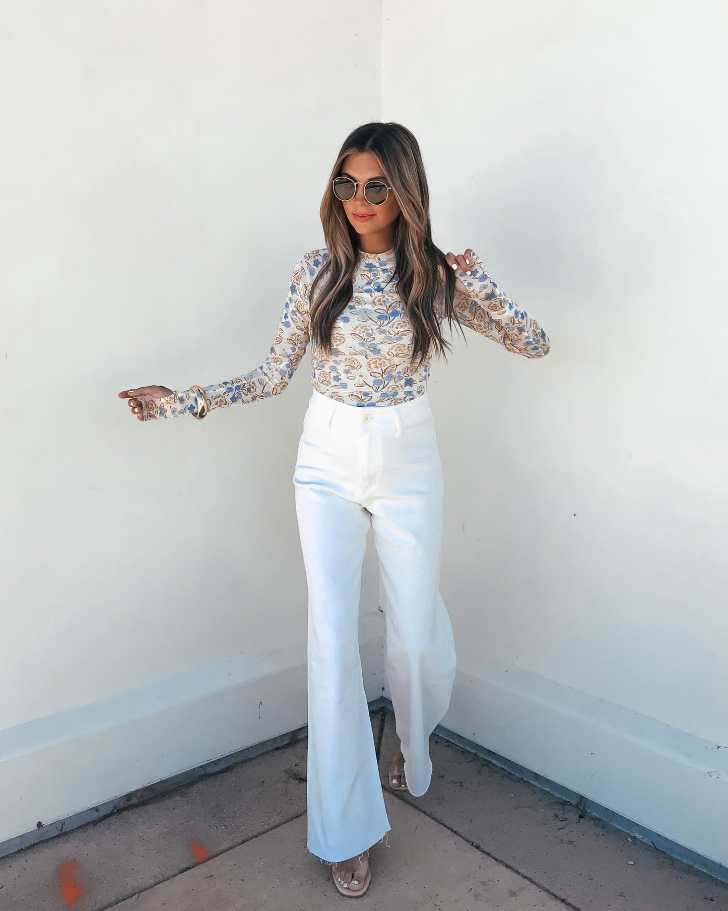 A woman in the Cream Floral Mesh Top, sunglasses, and white high-waisted pants stands against a white wall.