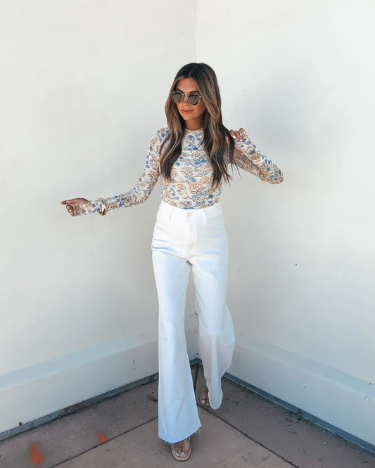 A woman in the Cream Floral Mesh Top, sunglasses, and white high-waisted pants stands against a white wall.