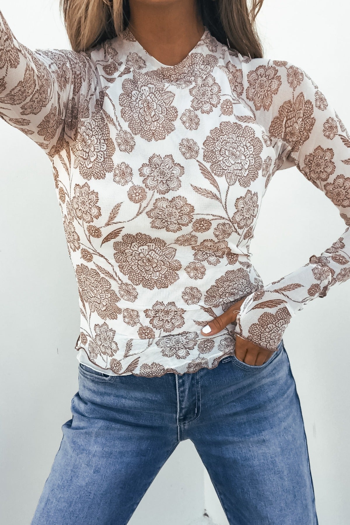 Model wears Cream Floral Mesh Top with blue jeans, posing confidently with one hand on her hip against a plain background.