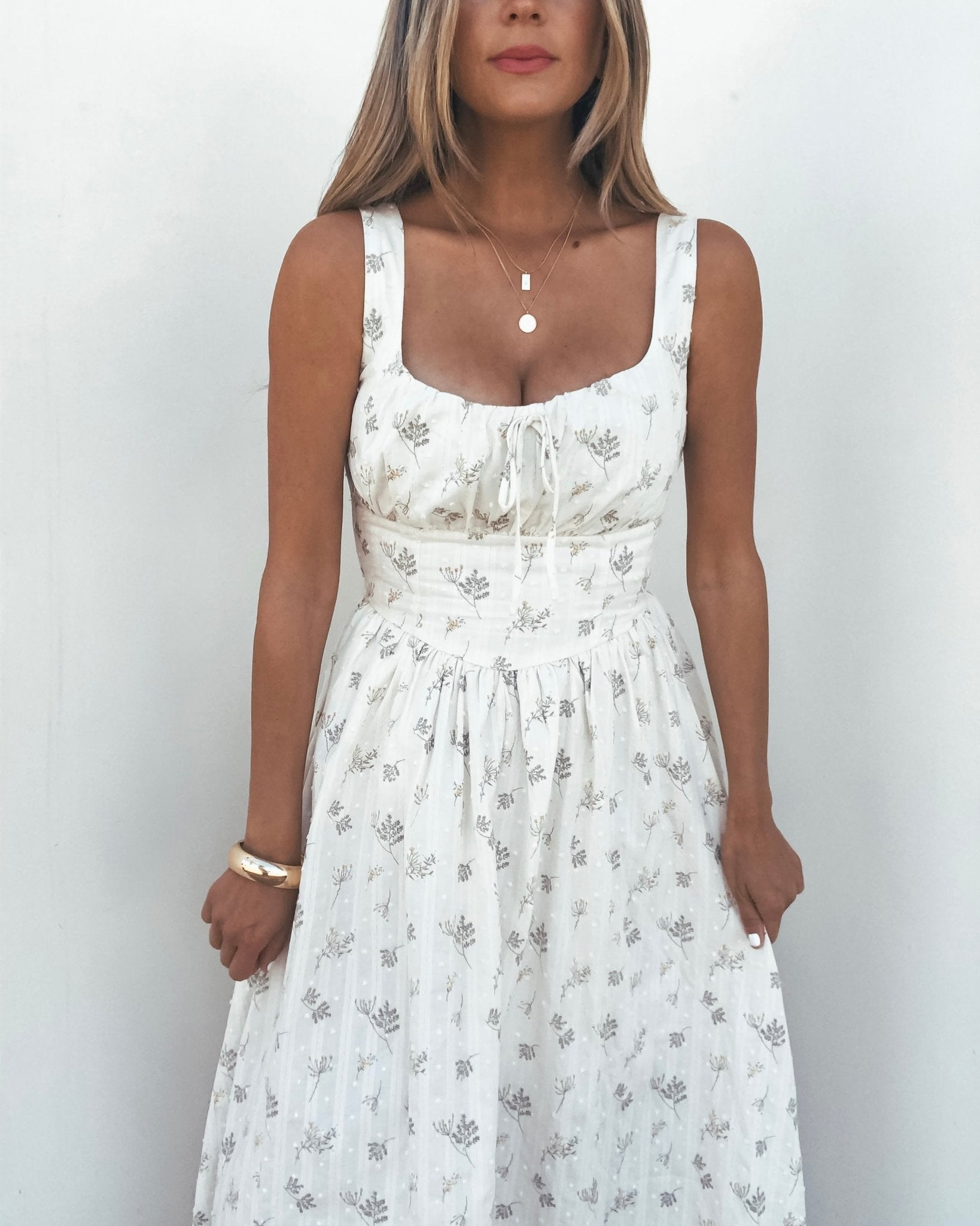 Woman wearing a Cream Floral Print Smocked Midi Dress with layered necklaces and a bracelet, standing against a white background.