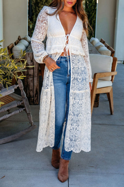 Woman in a Cream Lace Tie Duster Cardigan over a white top, blue jeans, and brown ankle boots, standing on a patio.
