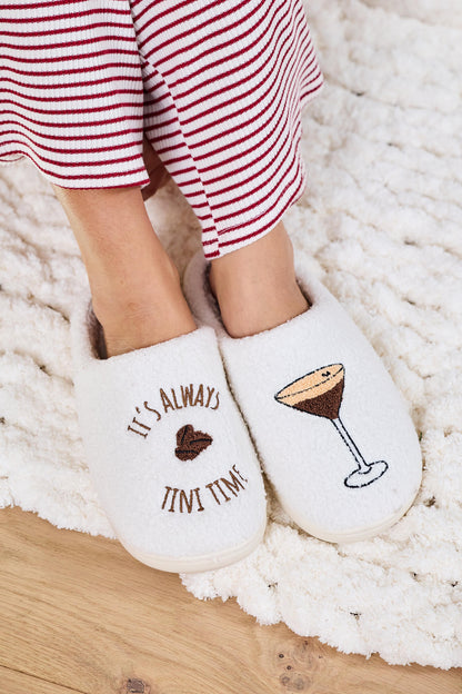 Person in striped pajamas relaxes on a white rug, wearing Cream Martini Plush Slippers-FINAL SALE—perfect for holiday gifting.