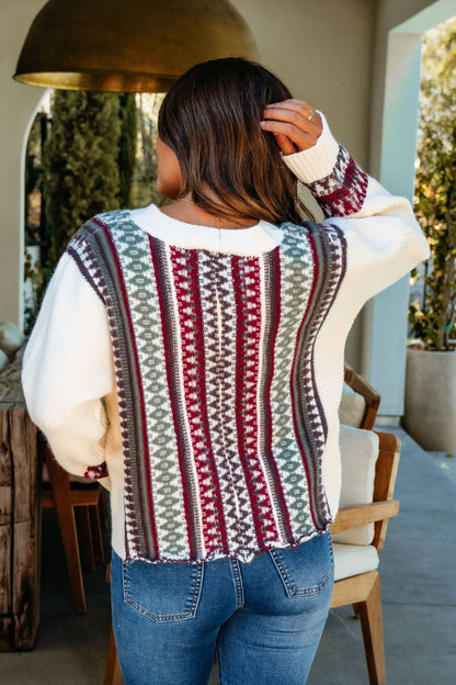A woman with brown hair wears the Cream Multi Ethnic Print Button Down Cardigan, facing away with one hand in her hair.