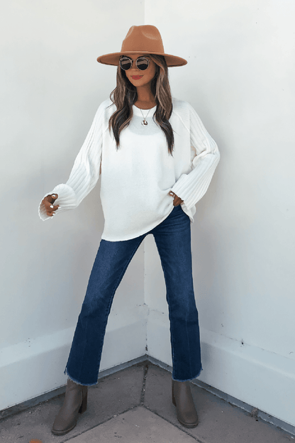 Woman in sunglasses, blue jeans, taupe boots, and a Cream Raglan Sleeve Textured Sweater poses confidently by a white wall.