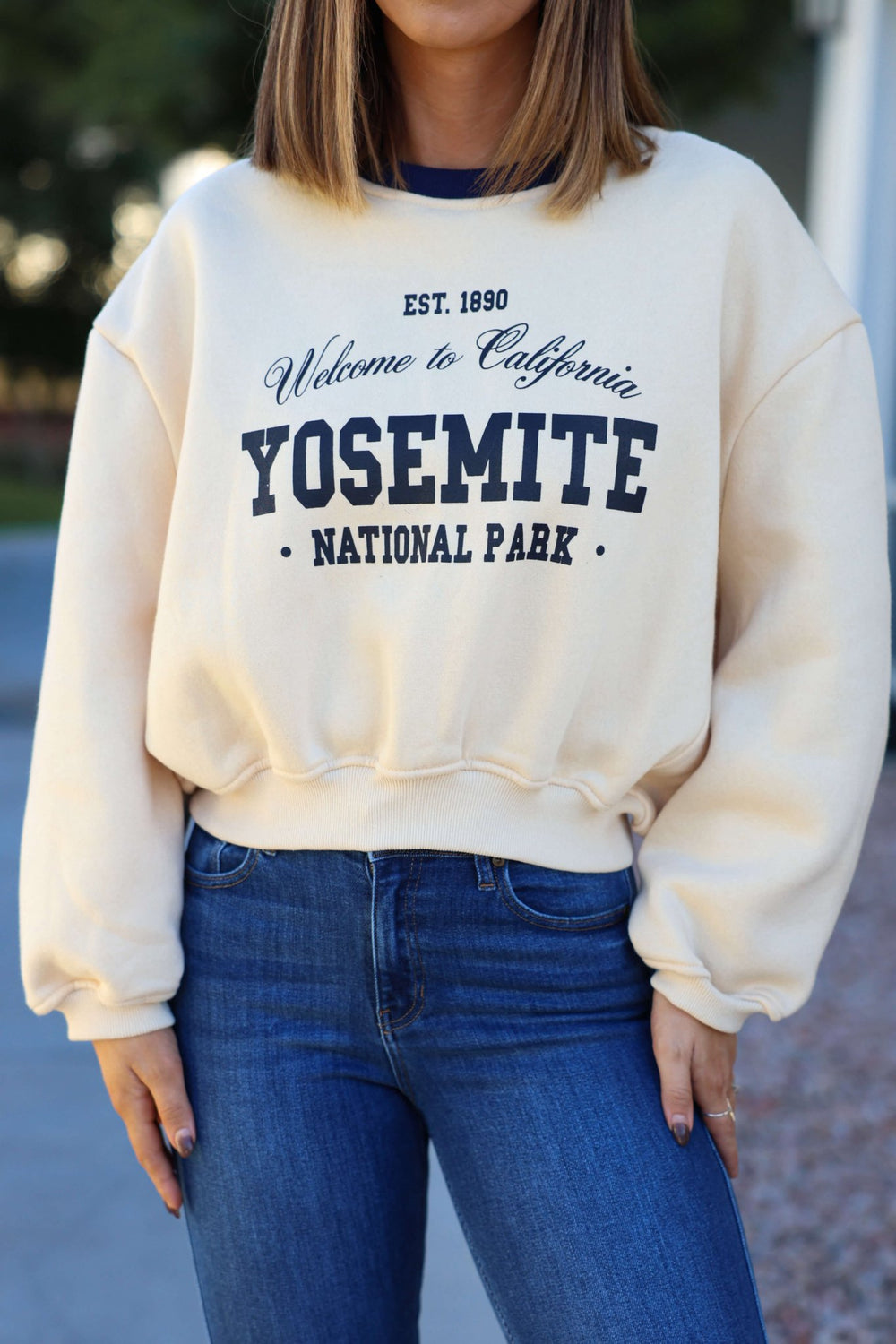 A woman wears the Cream Yosemite Graphic Crewneck Pullover (FINAL SALE) with blue jeans outdoors.