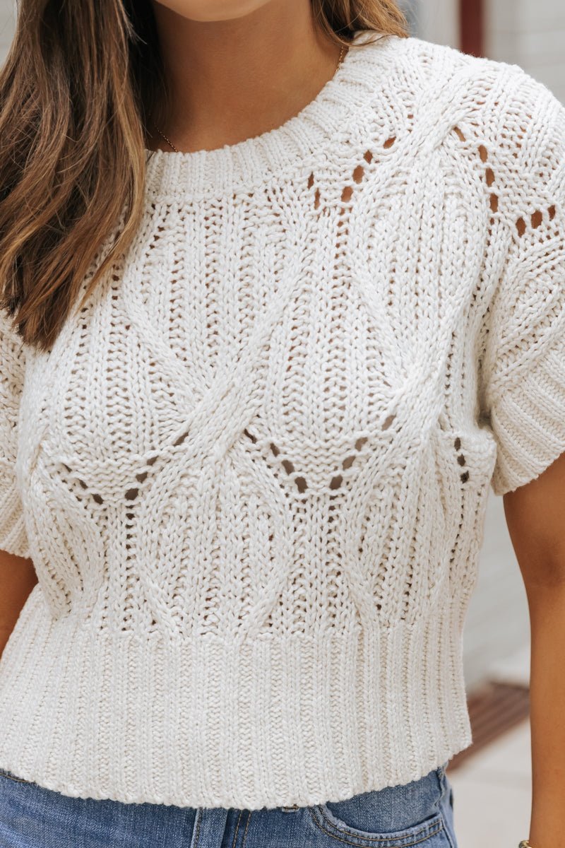 Woman wears an ivory Crochet Detail Short Sleeve Sweater paired with blue jeans.