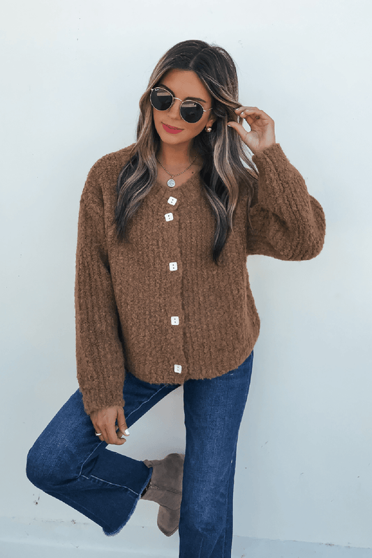 Woman in a Dark Amber Plush Button Down Cardigan, blue jeans, taupe boots, sunglasses, and red lipstick stands by a white wall.