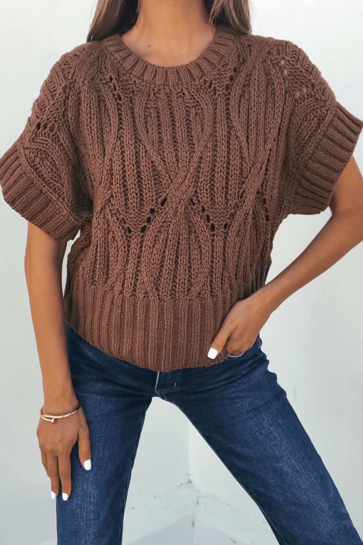 Woman in a Dark Brown Crochet Knit Sweater and blue jeans, posing with one hand on her hip—classic autumn style.