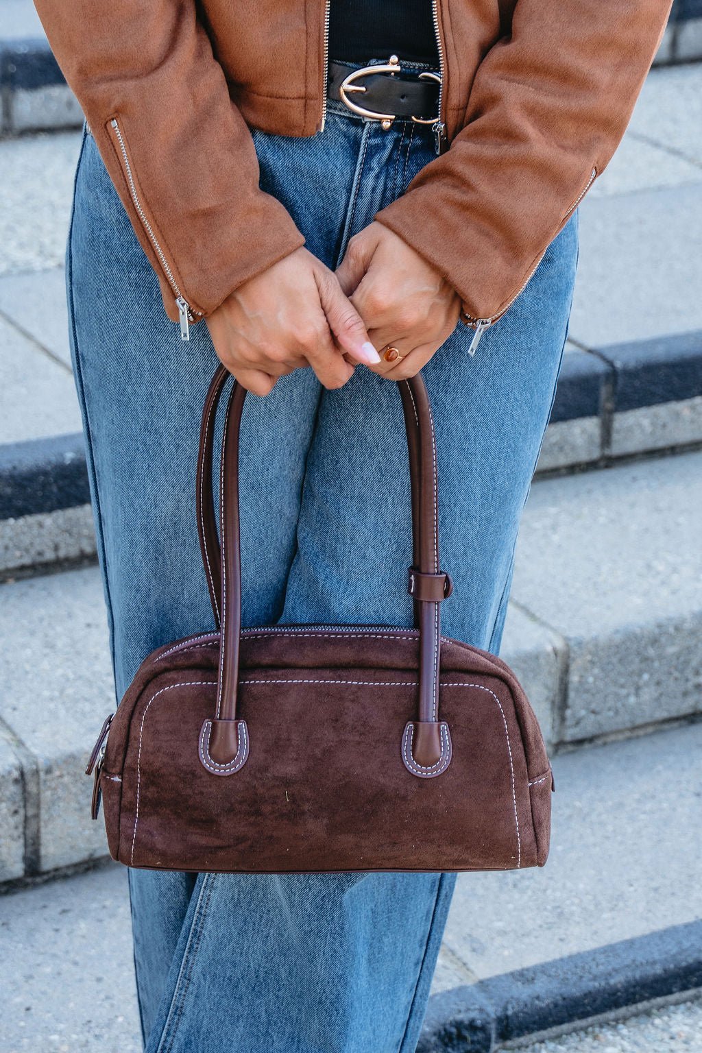 Person in a brown jacket and jeans holds the Dark Brown Faux Suede Baguette Bag while standing on outdoor steps.