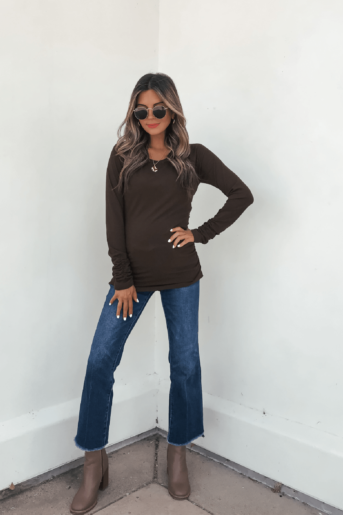 Woman poses confidently in sunglasses, blue jeans, and a Dark Brown Ruched Sleeve Ribbed Top with brown heeled boots.