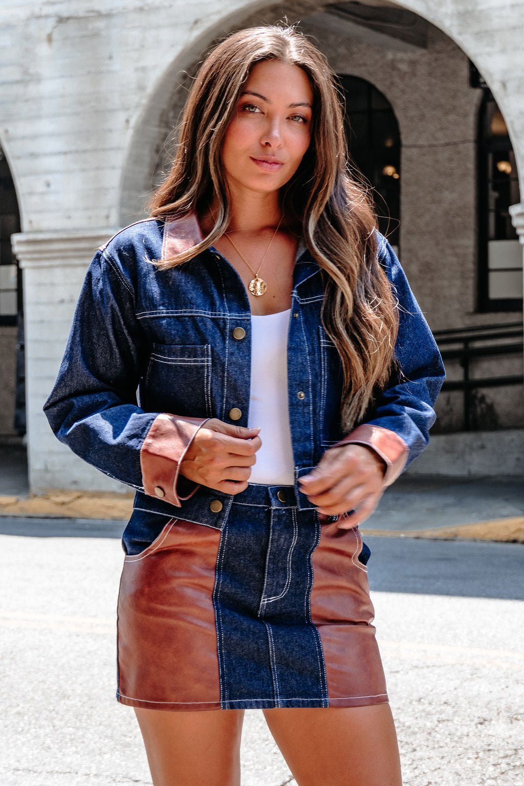 A woman wears the Dark Denim Contrast Mini Skirt - FINAL SALE, standing outdoors by an arched building.