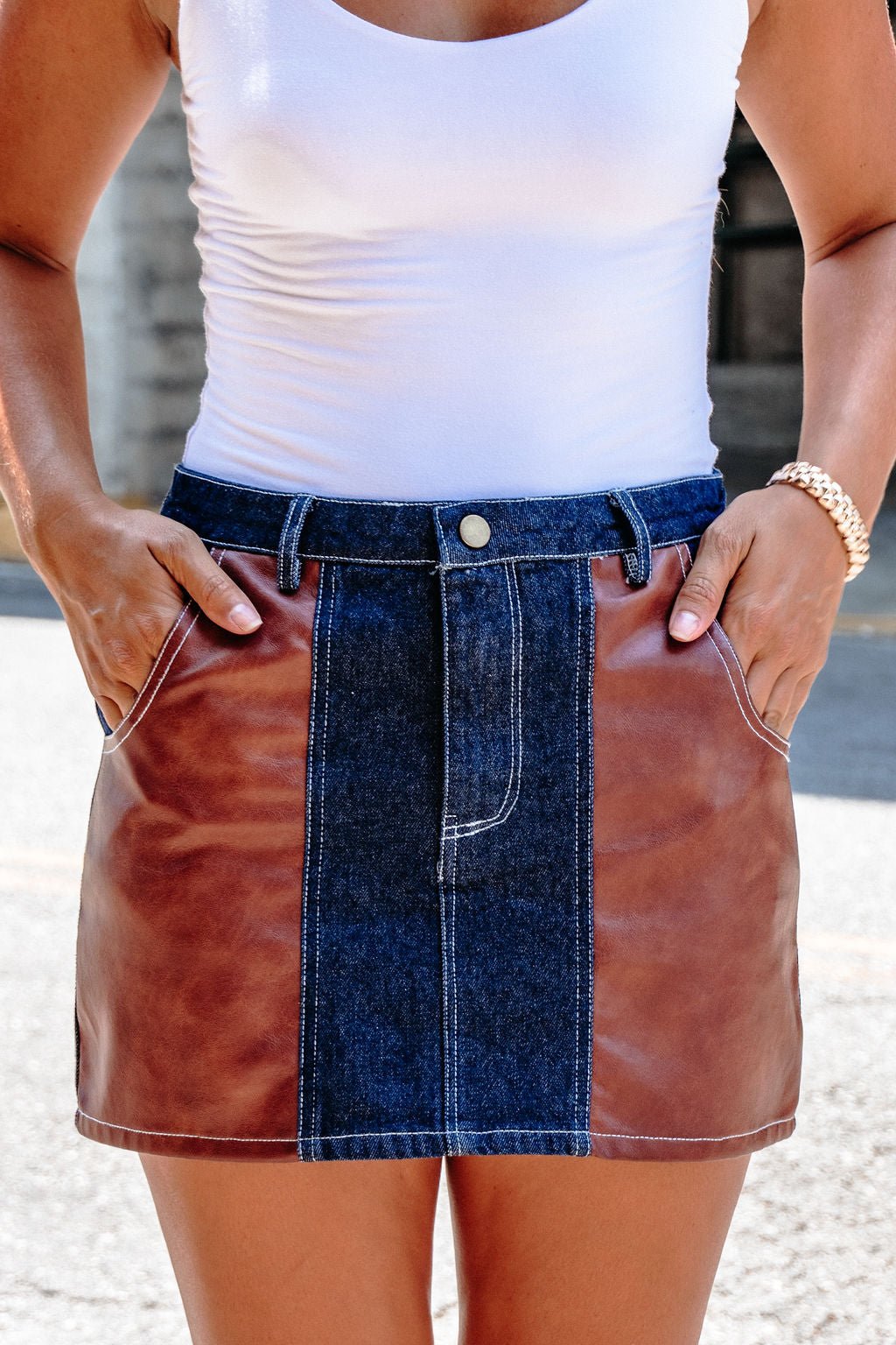 A woman wears a white tank top and the Dark Denim Contrast Mini Skirt - FINAL SALE, hands in pockets.